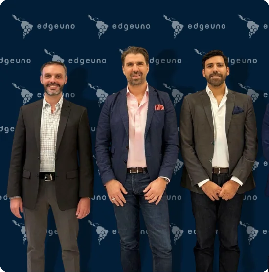 Three people posing at an EdgeUno events backdrop with EdgeUno logo wall.